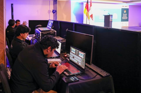 People working at computer stations in a gaming or esports facility with purple lighting and monitors displaying editing software