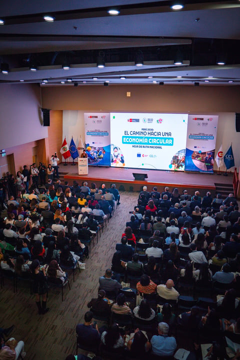 Large conference hall filled with attendees watching a presentation on circular economy on a main stage screen